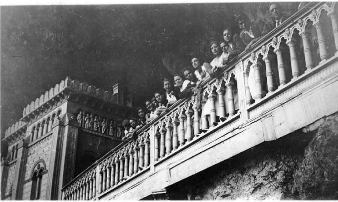 Grupo de hombres y mujeres asomados a la balaustrada de un castillo